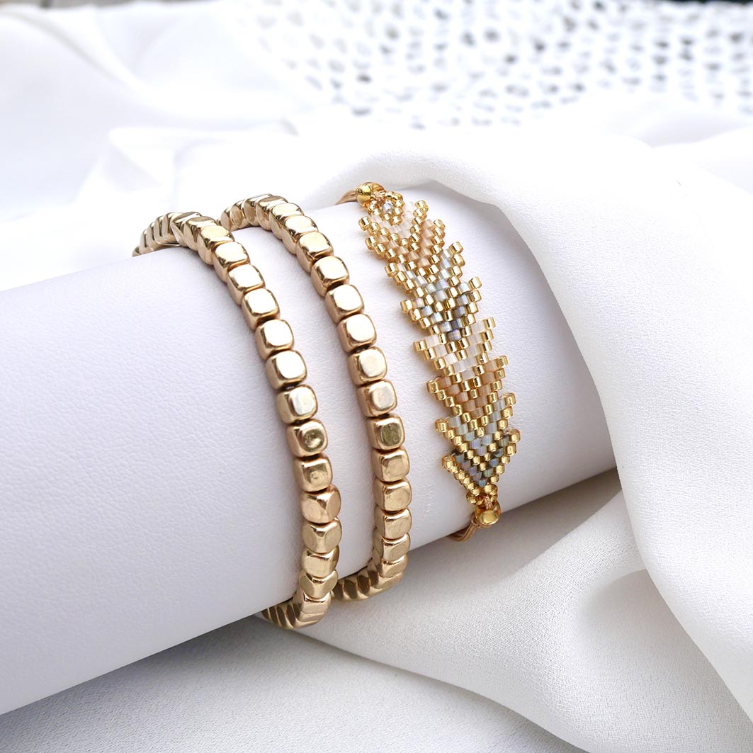 Trio de bracelets Golden Harmony en hématite dorée et chevron tissé sur fond blanc élégant